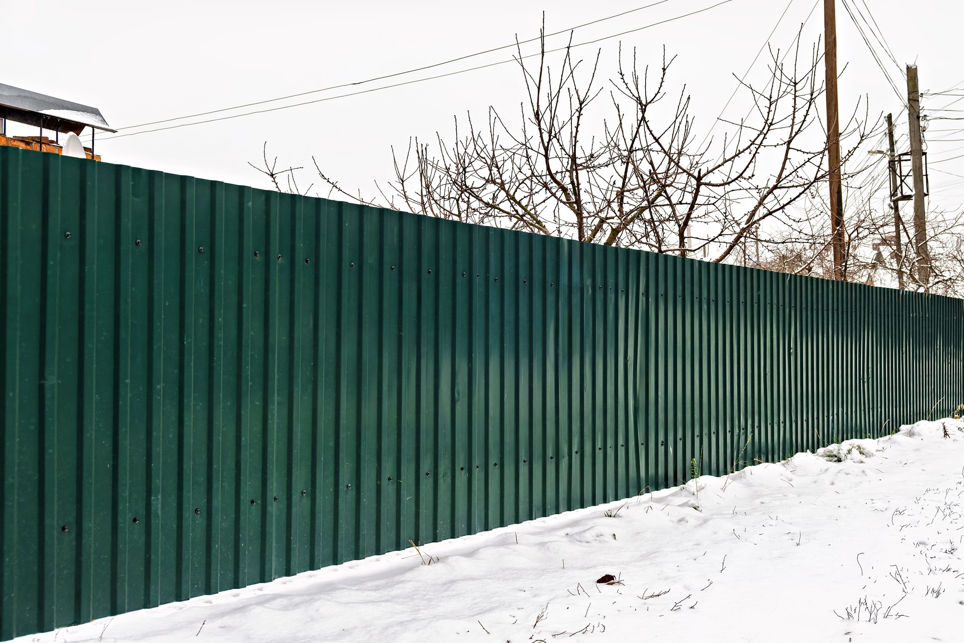 A green metal fence in the snow next to a house